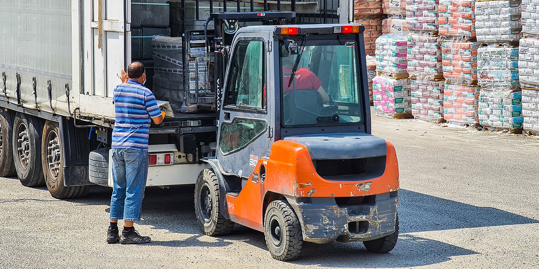 A forklift operator unloading a semi truck while a worker supervises nearby.