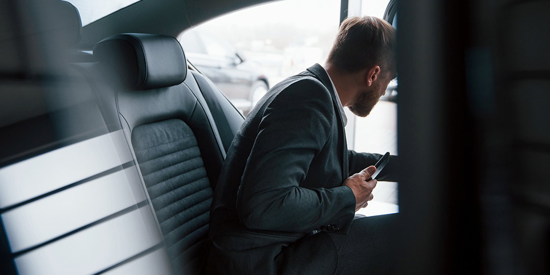 A man in a suit getting into the backseat of a rideshare vehicle.