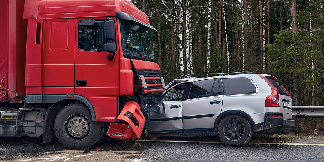 A large red truck and a gray van in a head-on collision on the road against a guardrail.