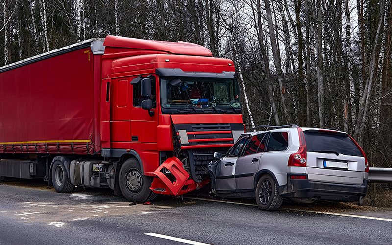 A grey SUV crushed by a large red semi-truck on a highway.