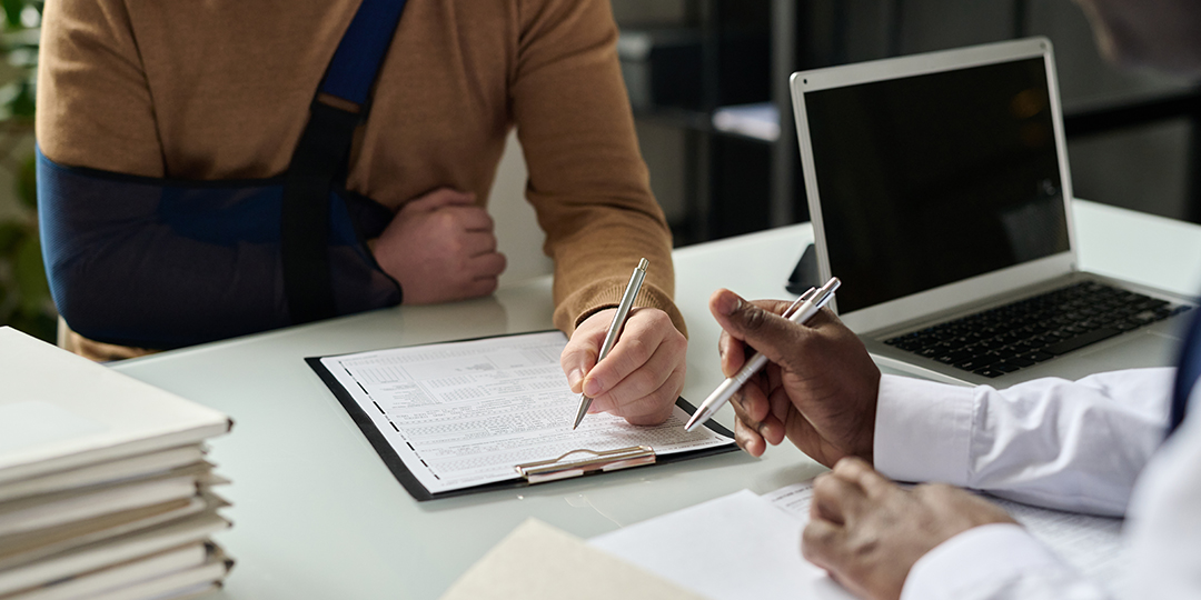 An injured client signing a document on a clipboard while meeting with an attorney.