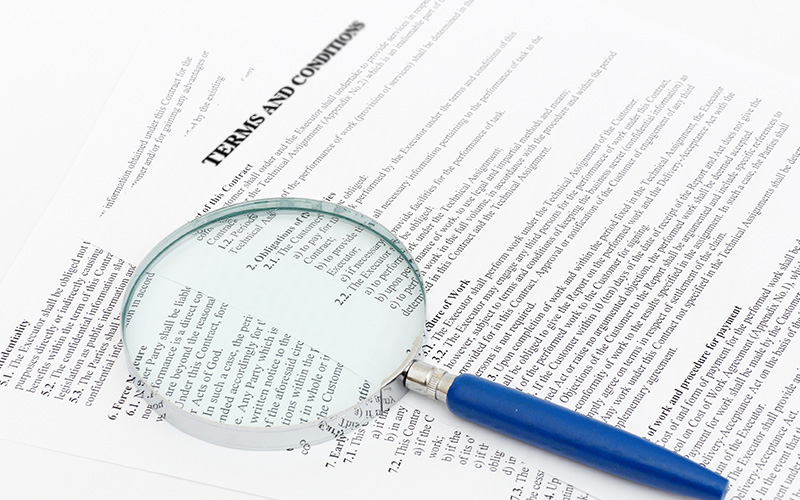 A magnifying glass laying on papers with long & detailed terms and conditions.