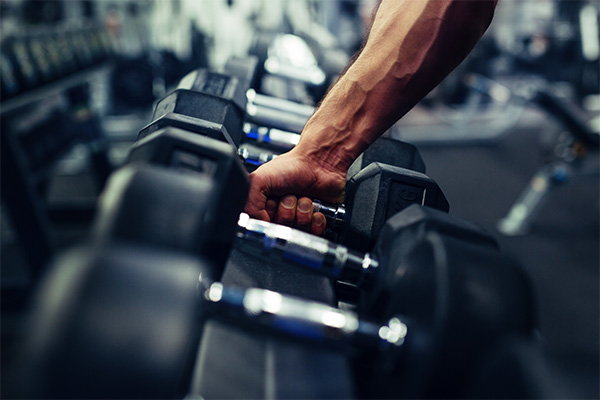 A man on Workers' Compensation picks up a dumbbell at a gym.