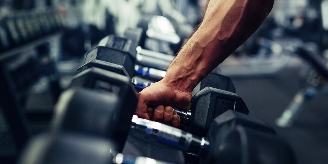 A man on Workers' Compensation picks up a dumbbell at a gym.