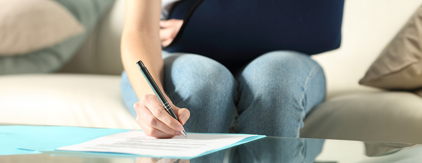 Injured woman with her arm in a sling using a pen to fill out paper work on a table.