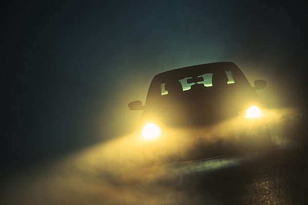 Bright headlights on a car shining in the dark fog.