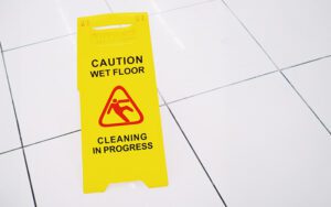 Bright yellow wet floor sign on a white tile floor, a potential fall hazard.