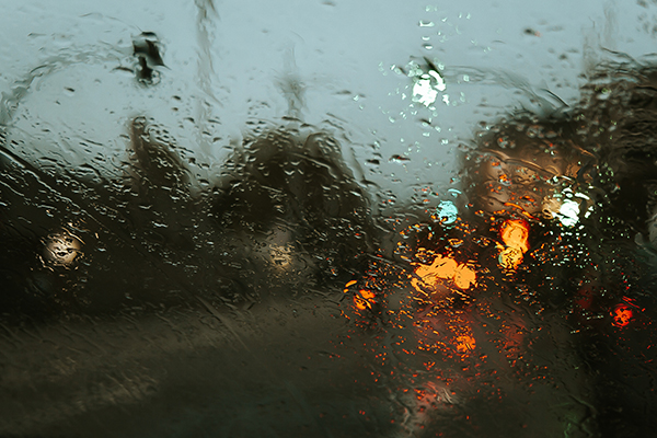 Blurry headlights and street lights viewed through a car windshield in the rain.