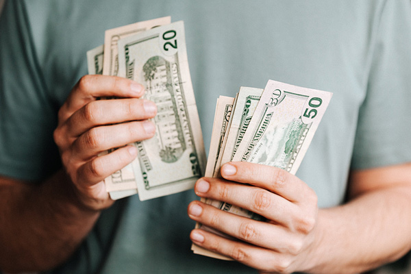 A man holding and counting several 20 dollar bills.