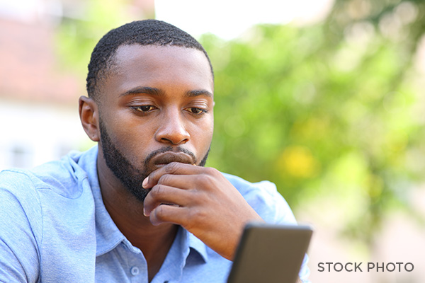 Black man looking regretfully with his hand on his chin at his phone.