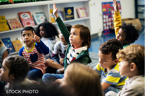 Students of different races/nationalities raise their hands in school.