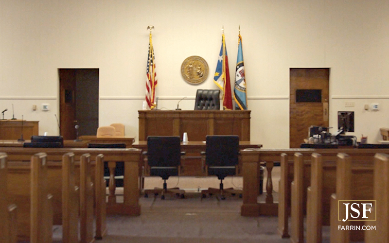 The interior of a North Carolina courtroom with flags and the state seal.
