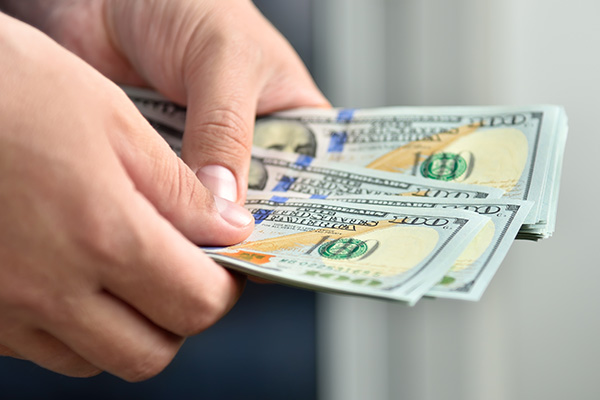 Close up of hands holding several 100 dollar bills.