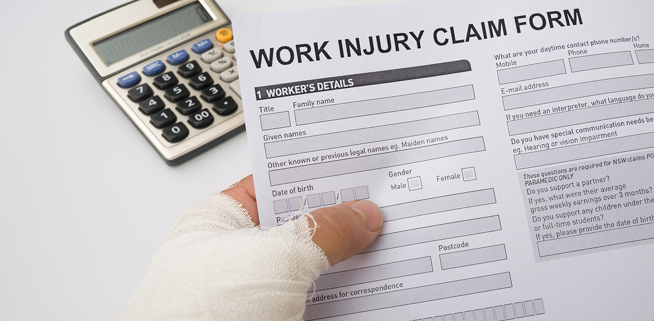 A bandaged hand holding workers' compensation forms with a calculator.