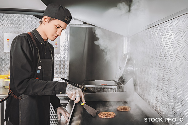 A young man cooking burgers on the grill in a fast food restaurant.