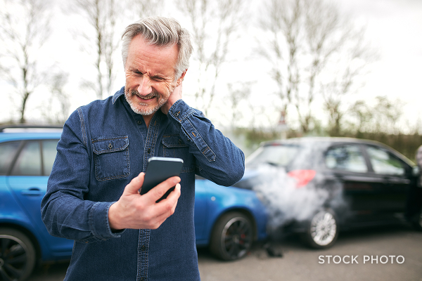 A man making a phone call while rubbing his sore neck wincing in pain after a car crash. James Scott Farrin, auto accident attorneys.
