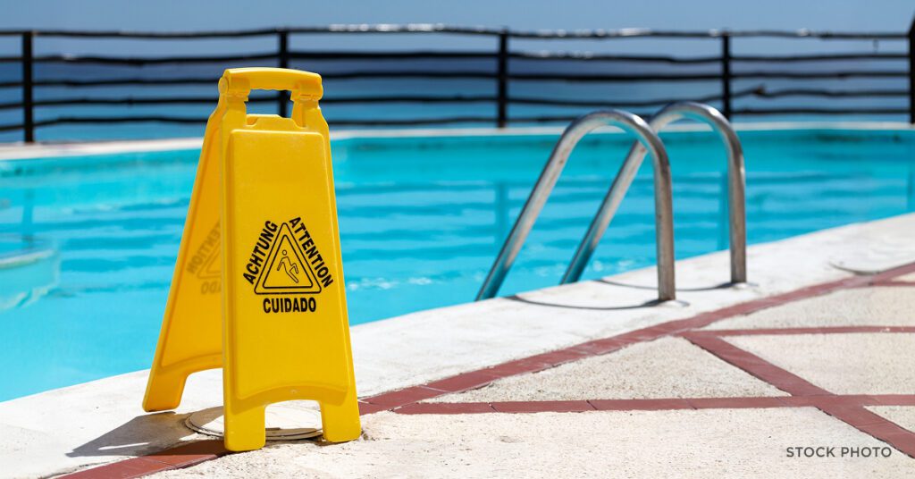Law Offices of James Scott Farrin North Carolina personal injury lawyers. Caution sign near pool edge highlighting slip hazard on wet surface.